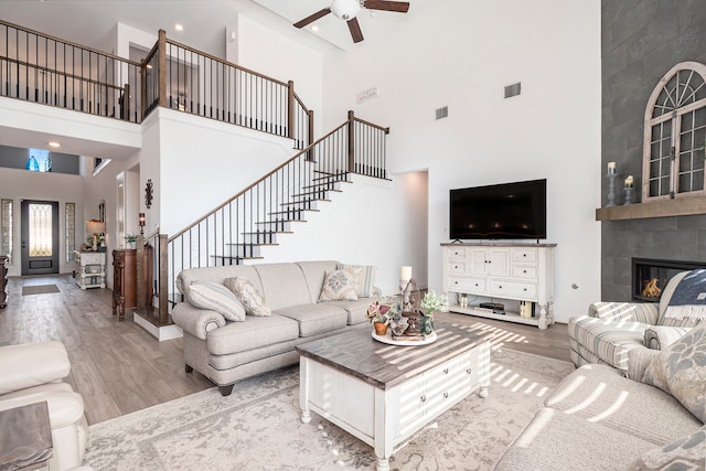 living room with a high ceiling, wood-type flooring, a tile fireplace, and ceiling fan