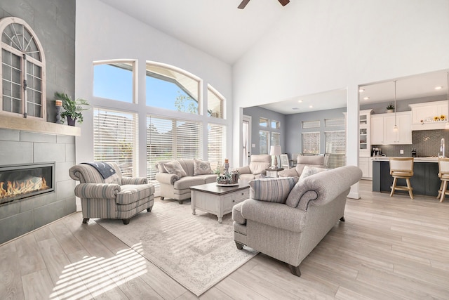 living room featuring a tiled fireplace, high vaulted ceiling, light hardwood / wood-style flooring, and ceiling fan