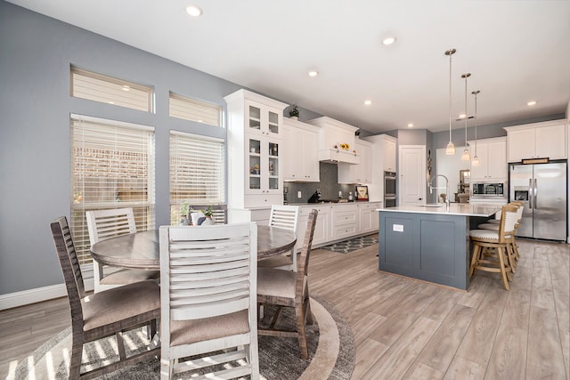 kitchen featuring an island with sink, white cabinets, decorative light fixtures, light wood-type flooring, and appliances with stainless steel finishes