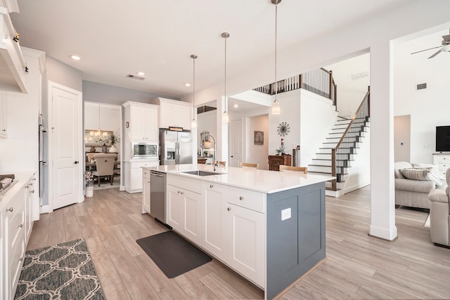 kitchen with hanging light fixtures, white cabinetry, stainless steel appliances, light hardwood / wood-style flooring, and a center island with sink