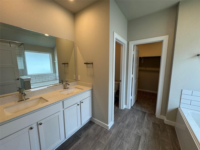 full bath with a sink, a bath, wood finished floors, and toilet