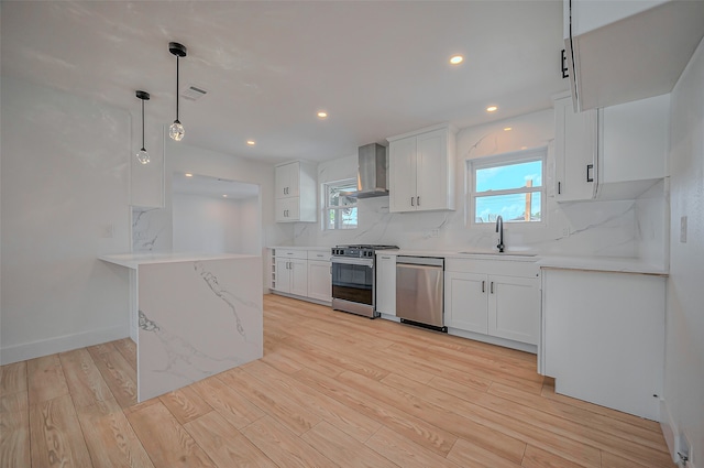 kitchen with wall chimney exhaust hood, hanging light fixtures, sink, white cabinetry, and appliances with stainless steel finishes