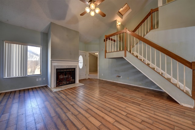 unfurnished living room featuring ceiling fan, a textured ceiling, hardwood / wood-style flooring, high vaulted ceiling, and a skylight