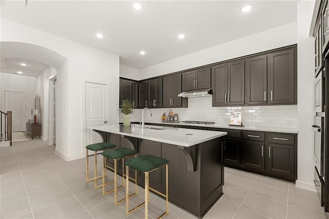 kitchen with light tile patterned floors, a center island with sink, a kitchen breakfast bar, stainless steel gas cooktop, and sink