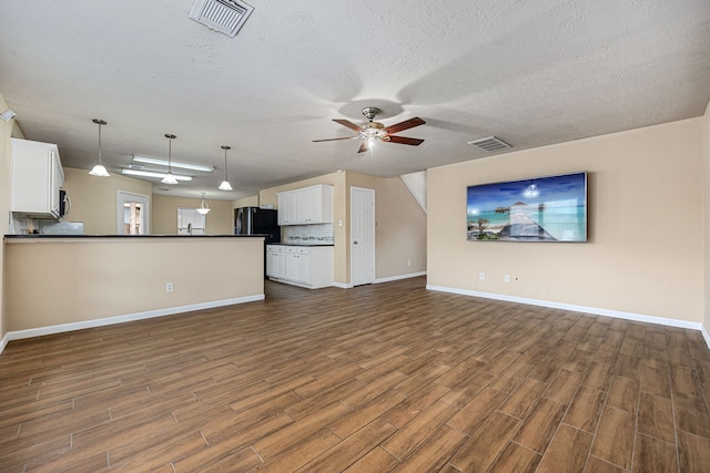 unfurnished living room with ceiling fan, a textured ceiling, and dark hardwood / wood-style flooring