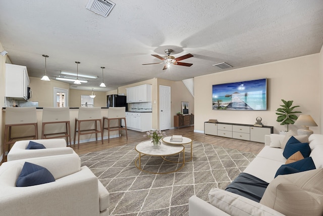 living room with ceiling fan, a textured ceiling, and hardwood / wood-style floors