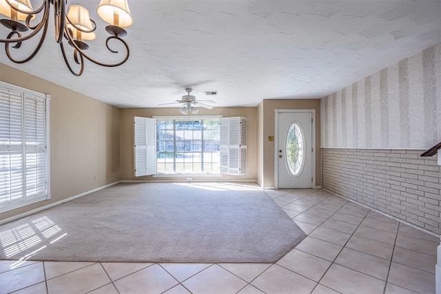 tiled foyer featuring brick wall and ceiling fan with notable chandelier