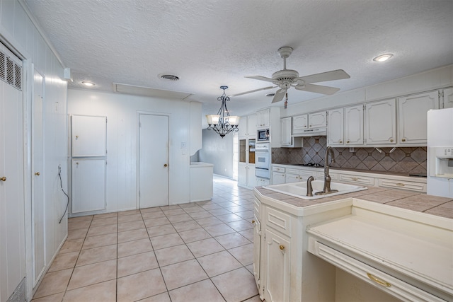 kitchen featuring tasteful backsplash, hanging light fixtures, light tile patterned floors, ceiling fan with notable chandelier, and tile counters