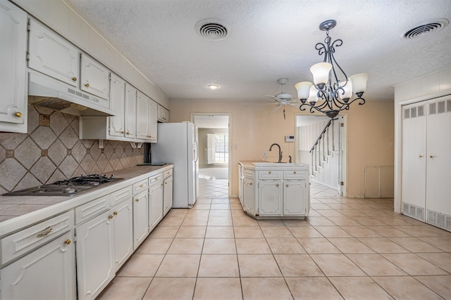 kitchen featuring stainless steel gas cooktop, decorative backsplash, white cabinets, and decorative light fixtures