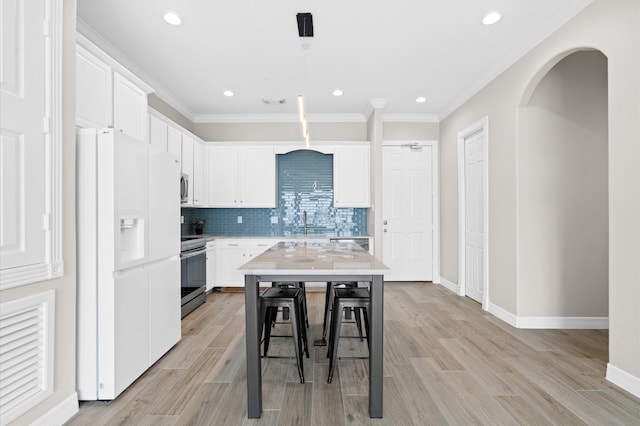 kitchen featuring white refrigerator with ice dispenser, stainless steel stove, a kitchen island, and white cabinets