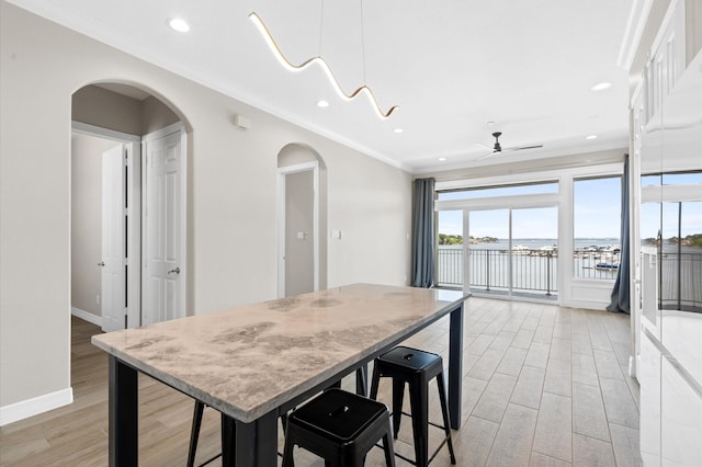 kitchen with ceiling fan, light hardwood / wood-style flooring, a breakfast bar area, a water view, and ornamental molding