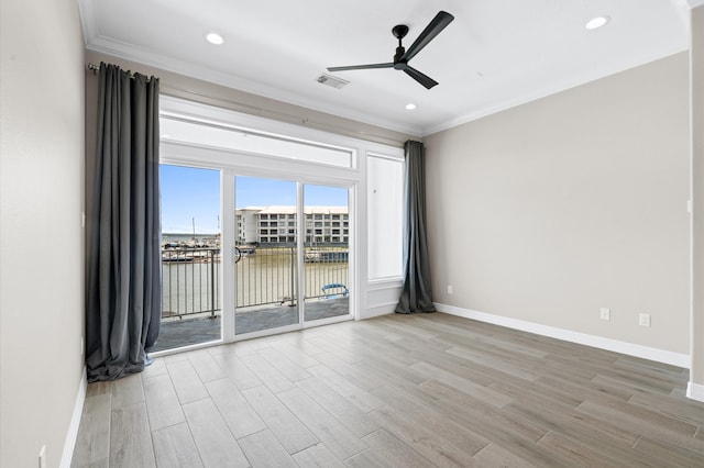 spare room featuring light wood-type flooring, a water view, ceiling fan, and ornamental molding