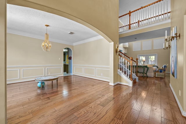 foyer entrance with an inviting chandelier, a textured ceiling, hardwood / wood-style flooring, a towering ceiling, and crown molding