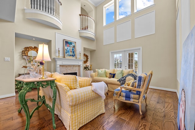 living room featuring french doors, hardwood / wood-style flooring, a towering ceiling, and a brick fireplace