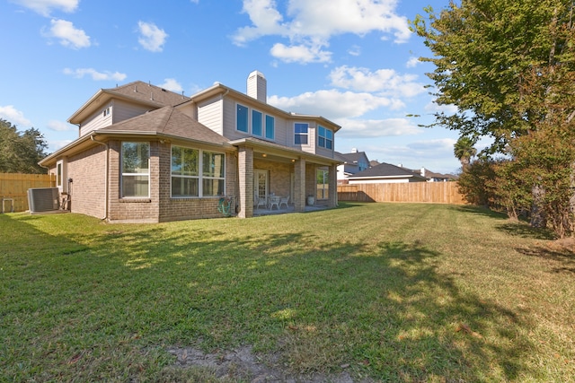 rear view of property with central air condition unit and a lawn