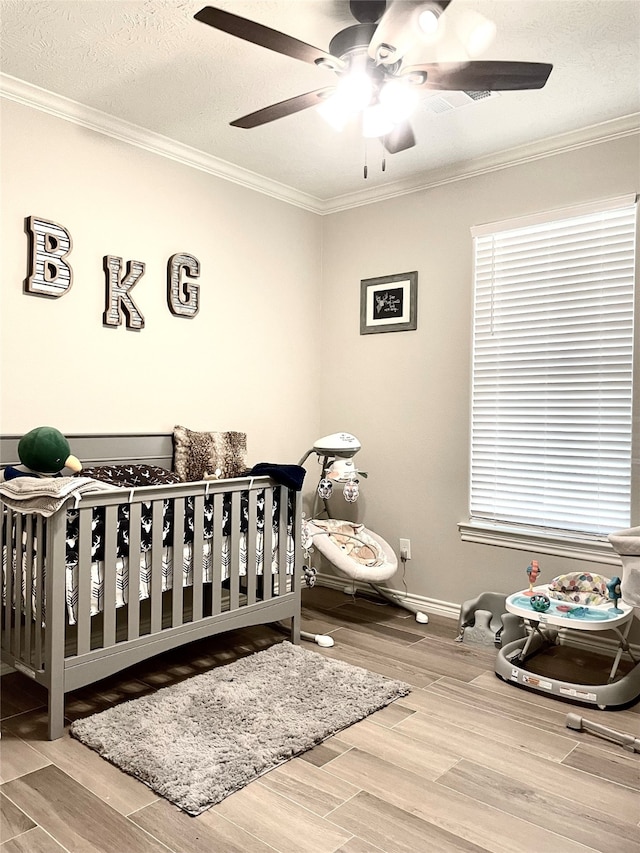 bedroom featuring hardwood / wood-style flooring, ornamental molding, ceiling fan, a textured ceiling, and a nursery area