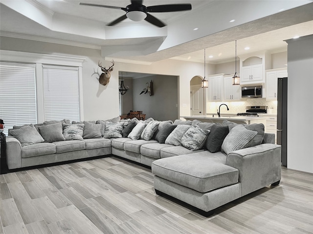 living room with sink, ceiling fan, a tray ceiling, crown molding, and light wood-type flooring