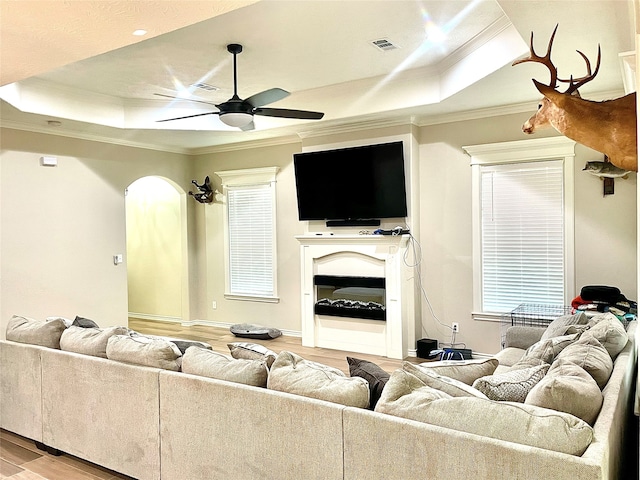 living room with ceiling fan, a raised ceiling, light wood-type flooring, and ornamental molding