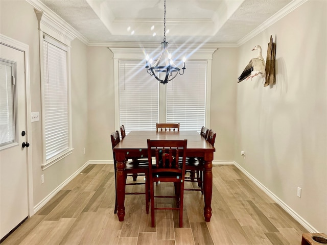 dining area featuring ornamental molding, an inviting chandelier, light hardwood / wood-style floors, and a raised ceiling