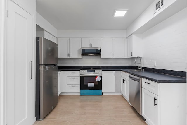 kitchen with white cabinets, sink, light hardwood / wood-style flooring, appliances with stainless steel finishes, and tasteful backsplash