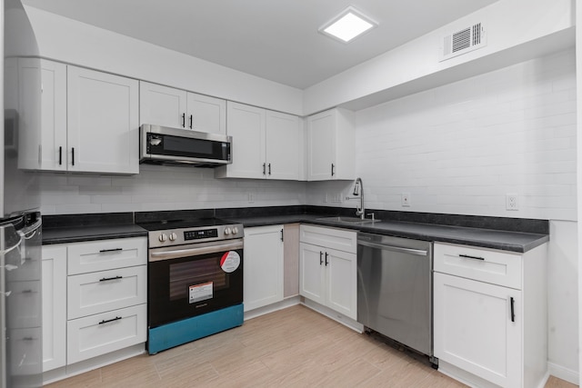 kitchen with appliances with stainless steel finishes, light wood-type flooring, tasteful backsplash, sink, and white cabinets