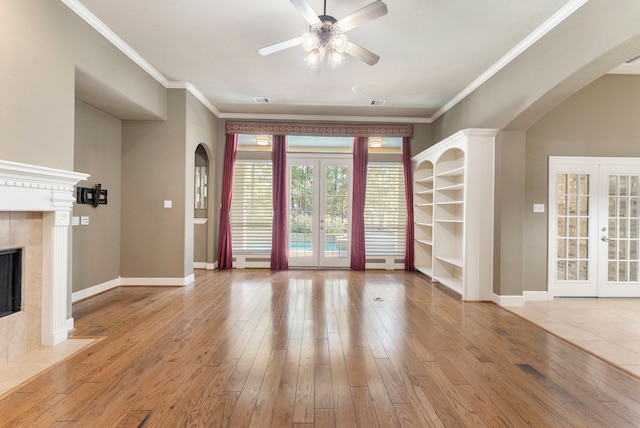 unfurnished living room featuring crown molding, light hardwood / wood-style flooring, ceiling fan, french doors, and a premium fireplace