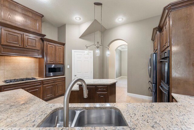 kitchen with light stone countertops, tasteful backsplash, sink, decorative light fixtures, and stainless steel appliances