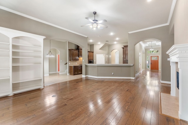 unfurnished living room with a fireplace, hardwood / wood-style floors, ceiling fan with notable chandelier, and crown molding