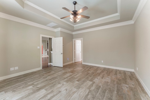 empty room with crown molding, light hardwood / wood-style flooring, ceiling fan, and a raised ceiling