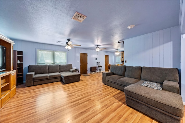 living room featuring light wood-type flooring, ceiling fan, and a textured ceiling