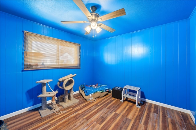 misc room with wooden walls, wood-type flooring, and ceiling fan