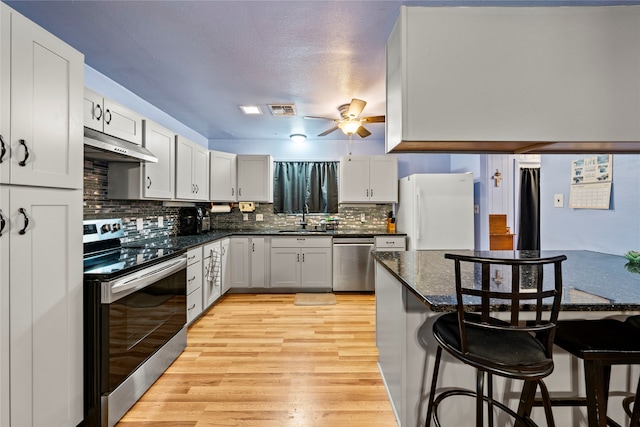 kitchen with appliances with stainless steel finishes, a kitchen bar, white cabinets, and light hardwood / wood-style floors