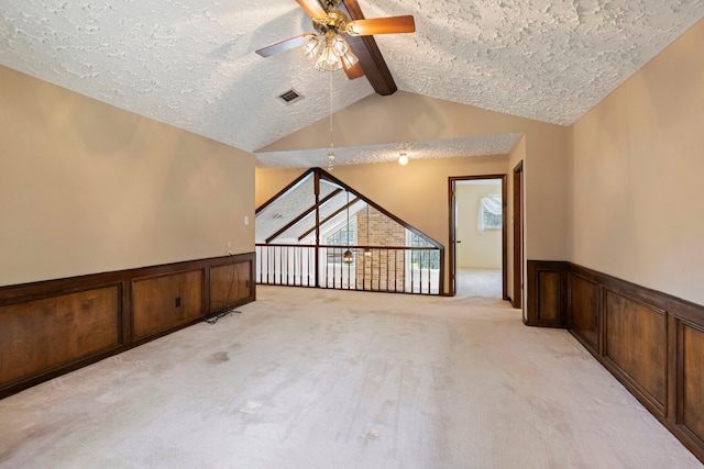 carpeted empty room with vaulted ceiling with beams, a textured ceiling, ceiling fan, and wooden walls