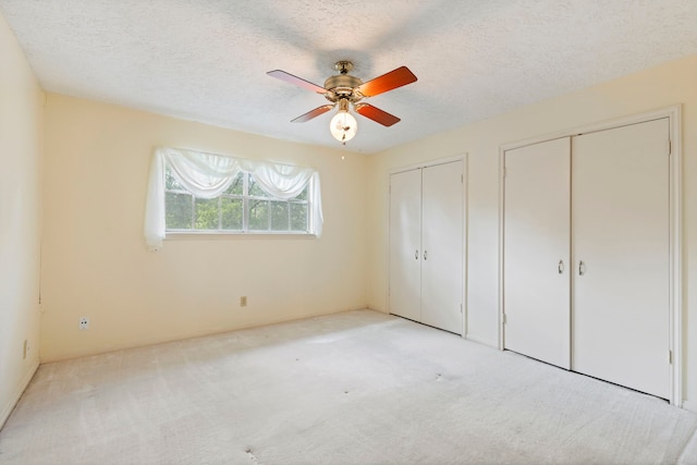 unfurnished bedroom with a textured ceiling, ceiling fan, light carpet, and two closets