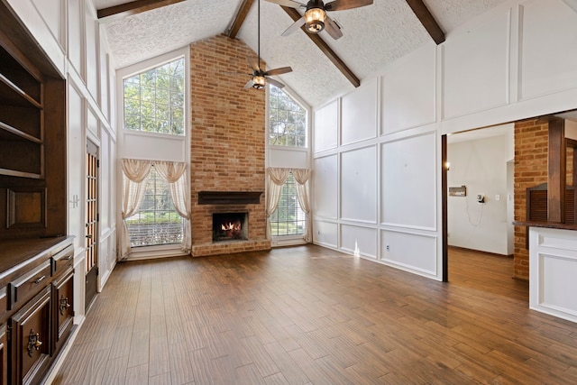 unfurnished living room featuring a textured ceiling, wood-type flooring, beam ceiling, high vaulted ceiling, and a fireplace