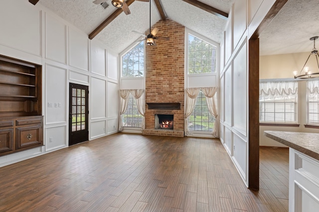 unfurnished living room with a fireplace, beam ceiling, high vaulted ceiling, and plenty of natural light