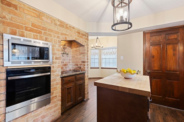 kitchen with dark wood-type flooring, decorative light fixtures, a kitchen island, stainless steel appliances, and a chandelier