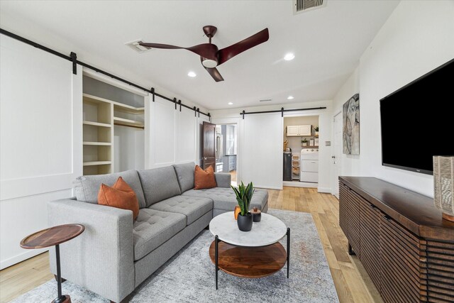 living room with independent washer and dryer, ceiling fan, a barn door, and light wood-type flooring