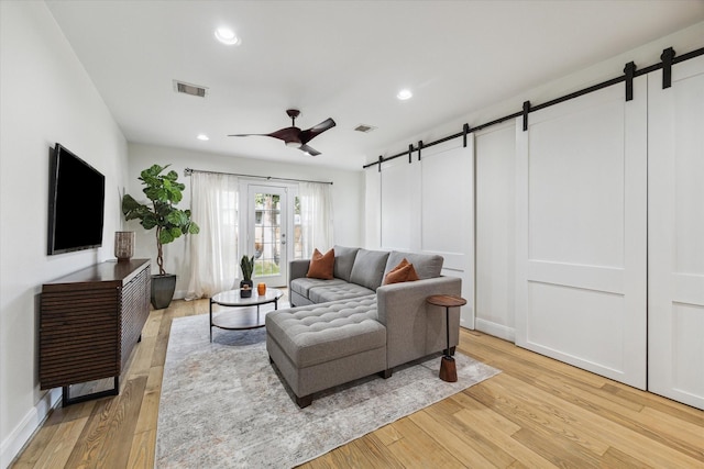 living room with light hardwood / wood-style flooring, a barn door, and ceiling fan