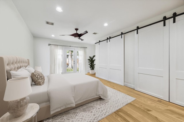 bedroom featuring a closet, a barn door, ceiling fan, and light wood-type flooring