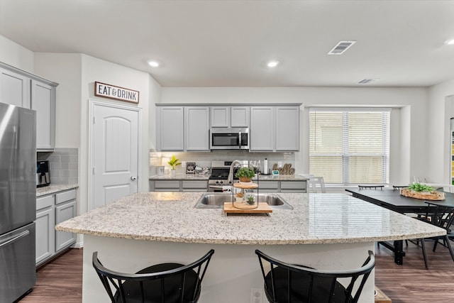 kitchen with dark wood-type flooring, a kitchen island with sink, stainless steel appliances, and backsplash