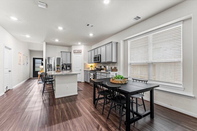 kitchen with appliances with stainless steel finishes, sink, gray cabinets, dark wood-type flooring, and a kitchen island with sink