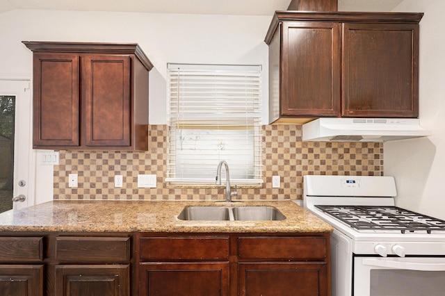 kitchen with white gas range oven, light stone counters, a sink, backsplash, and under cabinet range hood