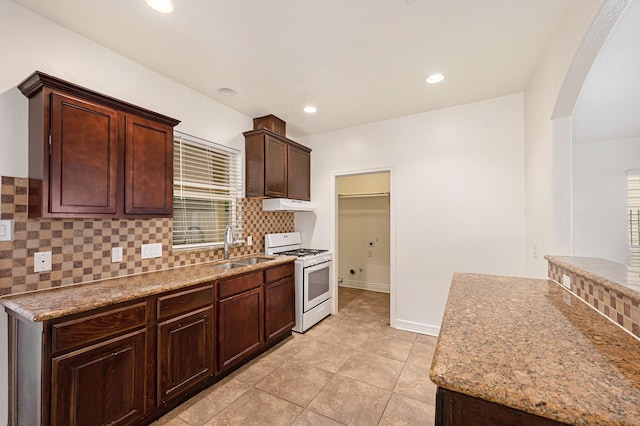 kitchen with decorative backsplash, a sink, white gas stove, under cabinet range hood, and arched walkways