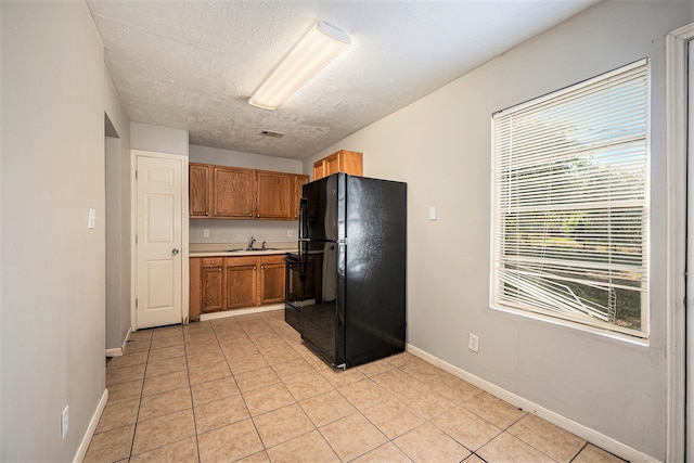 kitchen with a textured ceiling, light tile patterned flooring, black refrigerator, and sink