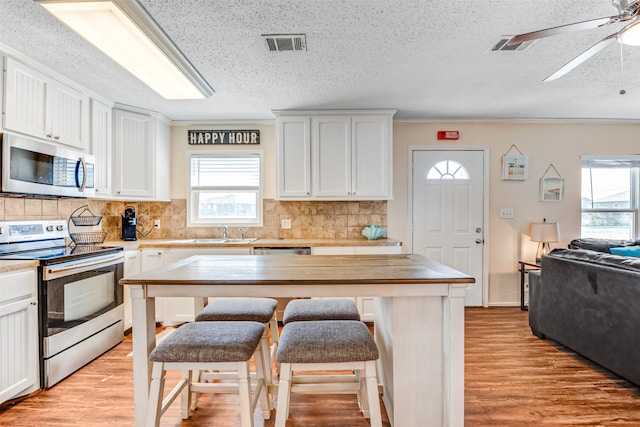 kitchen with appliances with stainless steel finishes, light wood-type flooring, a kitchen breakfast bar, and white cabinets