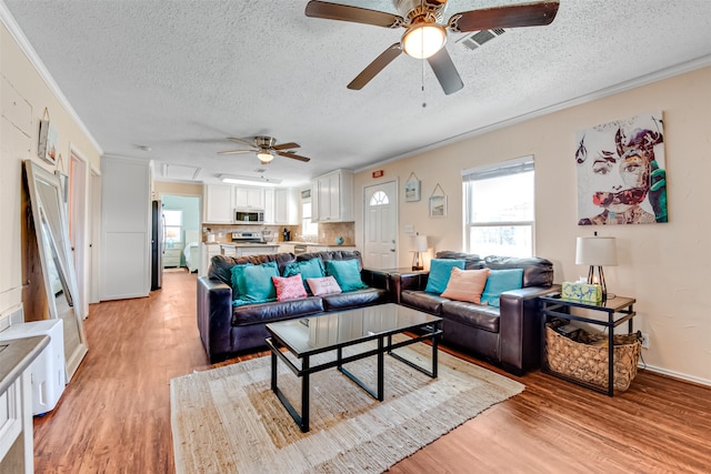 living room featuring crown molding, a textured ceiling, light wood-type flooring, and ceiling fan