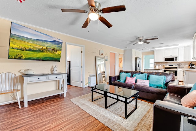 living room featuring ornamental molding, light hardwood / wood-style flooring, a textured ceiling, and ceiling fan