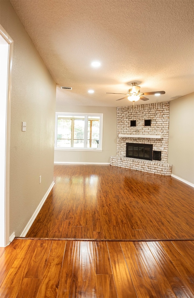 unfurnished living room featuring a textured ceiling, hardwood / wood-style flooring, a fireplace, and ceiling fan