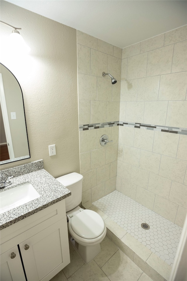 bathroom featuring vanity, tile patterned flooring, toilet, and tiled shower